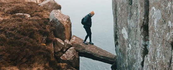 Beheerd beleggen: bergwandelaar loopt voorzichtig over natuurlijke brug over ravijn.